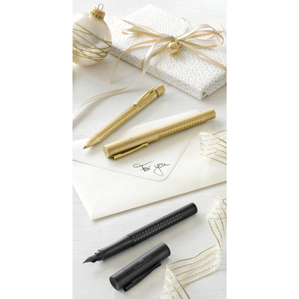 Schwarzer Füllfederhalter neben goldenen Stiften und verpacktem Geschenk auf einem Tisch.