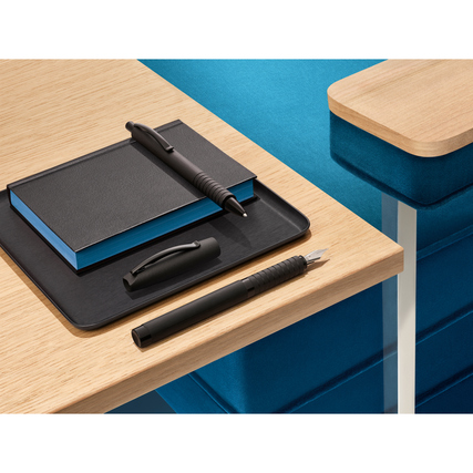 Füllfederhalter und Notizbuch liegen auf einem Schreibtisch mit einem schwarzen Tablett.