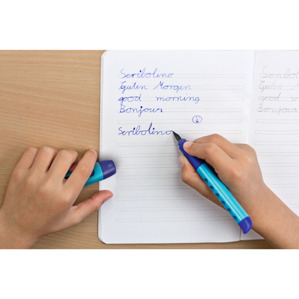 Füllfederhalter Scribolino in blau in der Hand eines Kindes beim Schreiben in ein Notizbuch.
