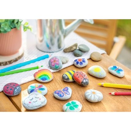 Buntstifte liegen auf einem Tisch neben bemalten Steinen und einer Gießkanne.