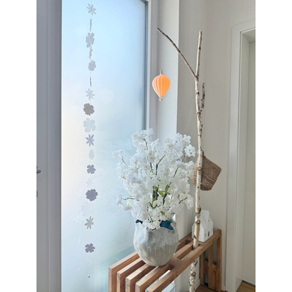 Lampenschirm Paulina in orange hängt neben einer Blumenvase mit weißen Blumen in einem hellen Raum.