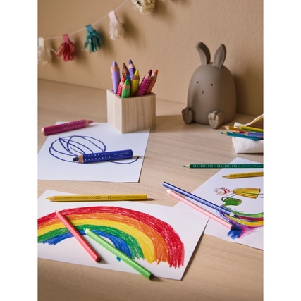 Faber-Castell Buntstifte liegen auf einem Tisch mit bunten Zeichnungen und einem Dekorationsobjekt.