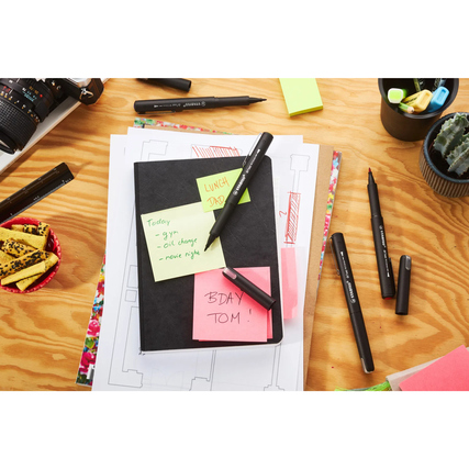 Fasermaler in Schwarz, Blau, Rot und Grün liegen auf einem Tisch mit Notizbuch und Post-its.