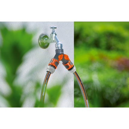 GARDENA 2-Wege-Verteiler mit zwei Schlauchanschlüssen am Wasserhahn in einer grünen Gartenumgebung.