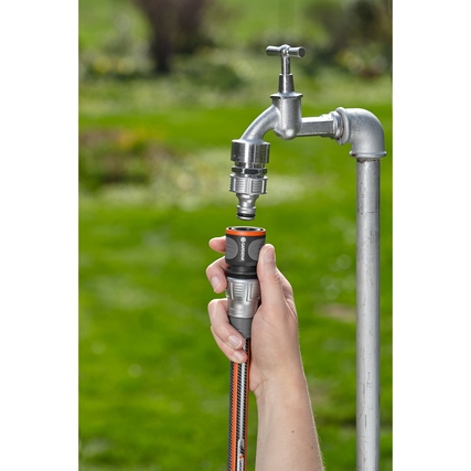 Hochwertiger Schlauchverbinder in Hand, angeschlossen an einen Wasserhahn im Freien.