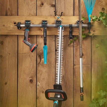 GARDENA Heckenschere EasyCut 55/18V hängt zusammen mit anderem Gartenzubehör an einer Holzwand.