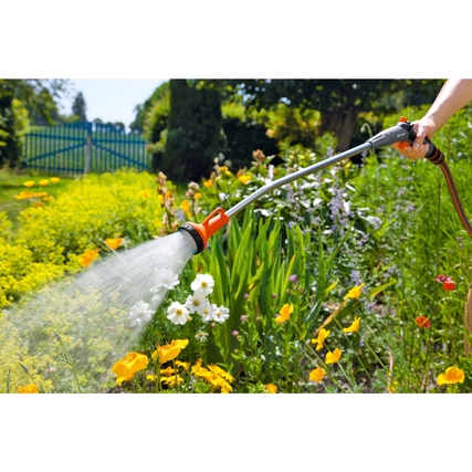 Gießstab im Einsatz zur Bewässerung von Blumenbeeten in einem Garten.