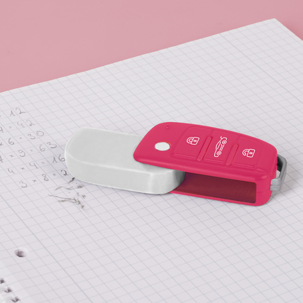 Weißer Radiergummi mit pinker Klappmechanik in Form eines Autoschlüssels auf einem Notizblock.