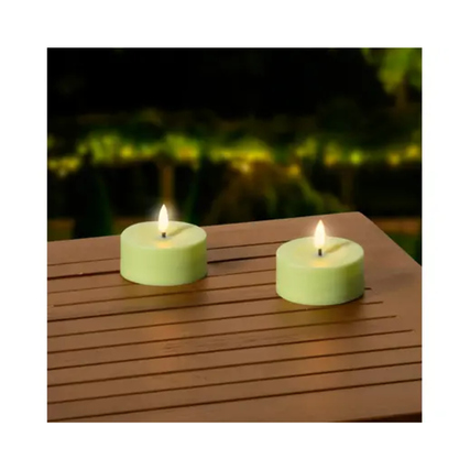 Zwei grüne, runde Solarleuchten mit warmem Licht auf einem Holztisch im Außenbereich.