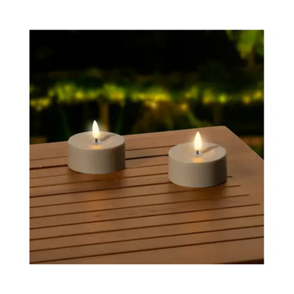 Zwei Teelichter auf einem Holztisch im Außenbereich, mit warmem Licht und dekorativer Atmosphäre.