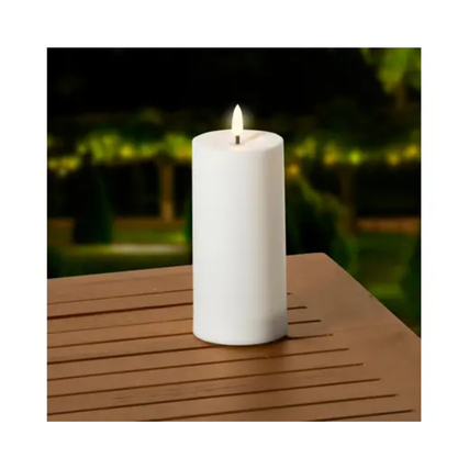 Weiße Solarleuchte im Kerzendesign auf einem Tisch, mit warmem Lichtstrahl oben.