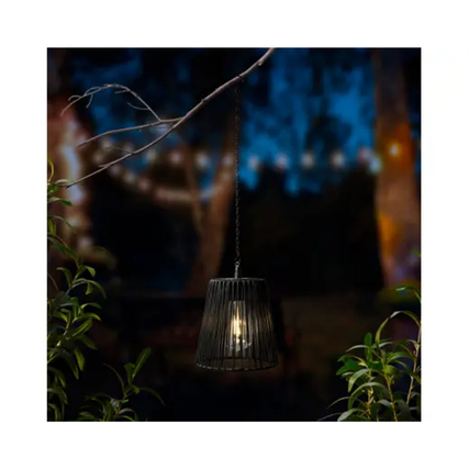 Schwarze Hängeleuchte hängt an einem Ast, beleuchtet eine Gartenlandschaft bei Nacht.