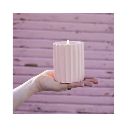 LED-Kerze in hellrosa, gehalten in der Hand vor einer pinken Wand, mit flammensicherem Licht.