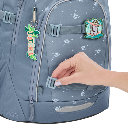 Schulrucksack MATE Bloomy Daisy in Grau mit anpassbaren Clips und Anhängern, Hand greift nach Clip.