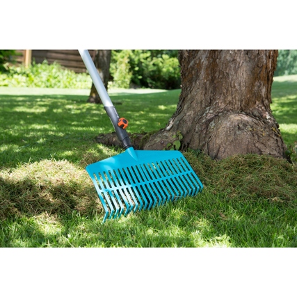 Teleskop-Rechenbesen auf Rasen unter einem Baum, zur Zusammenreinigung von Gartenabfällen.