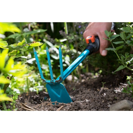 GARDENA Kleinhäckchen mit drei Zinken und Blatt zur Bodenbearbeitung in einem Gartenbeet.