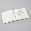 Offenes Gästebuch mit leeren Seiten und handschriftlichem Text auf grauem Untergrund.