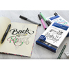 Set aus Tuschestiften auf einem Tisch mit einer geöffneten Skizze und einem Hand Lettering Booklet.