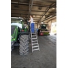 Person steht auf einer Stehleiter und arbeitet an einem Traktor in einer Werkstatt.